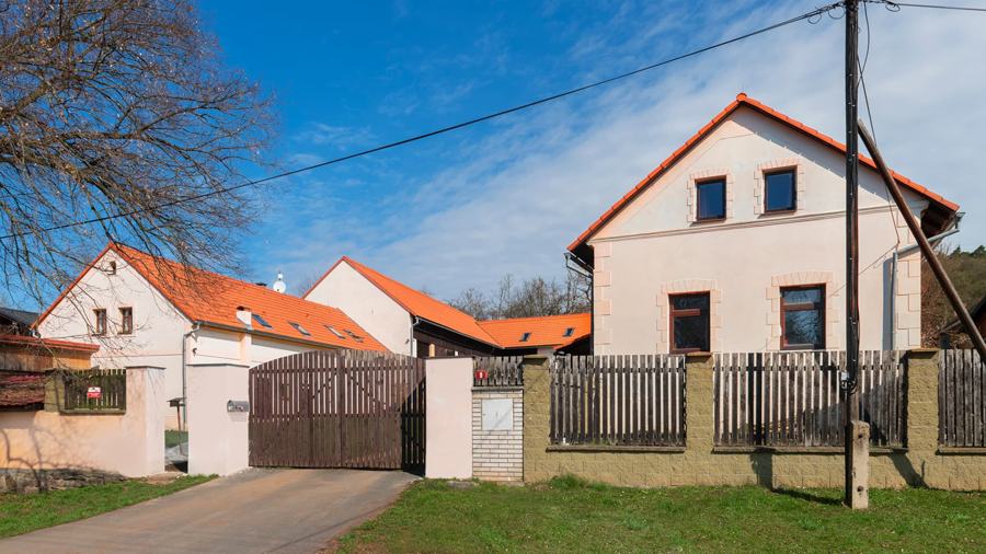 Chalupa s dřevěnou bránou a plotem u vesnické silnice